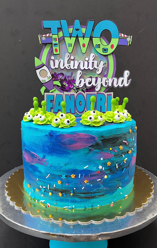 A cake with a blue and purple themed icing and a green cake topper with the text 'TWO infinity beyond' and decorative elements.
